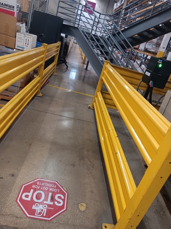 A guarded pedestrian route beside a mezzanine stair in a distribution center
