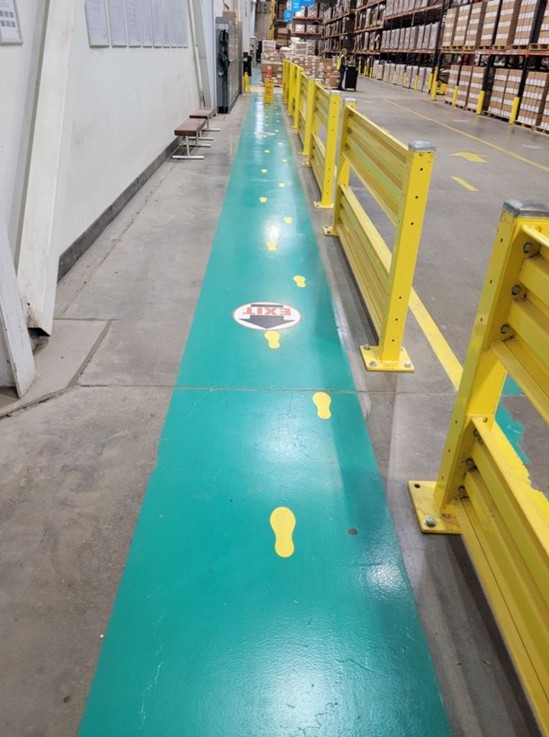 A marked green pedestrian walkway running alongside racking in a warehouse