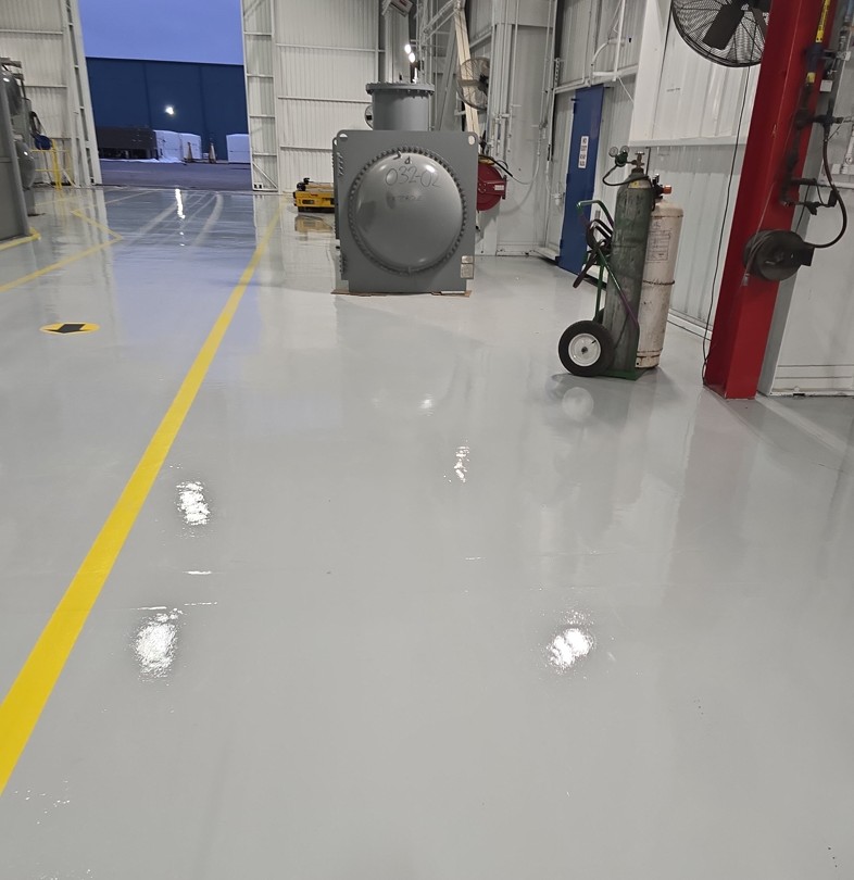 An epoxy coated equipment bay floor at an HM Solutions account, reflecting the overhead lights, with yellow lane striping