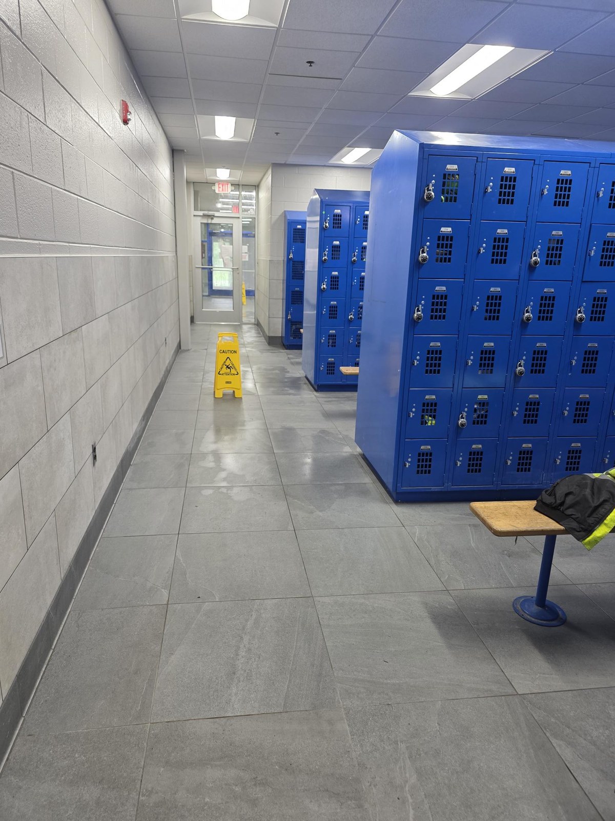 A locker room corridor at an HM Solutions account, freshly mopped with a caution wet floor sign in place